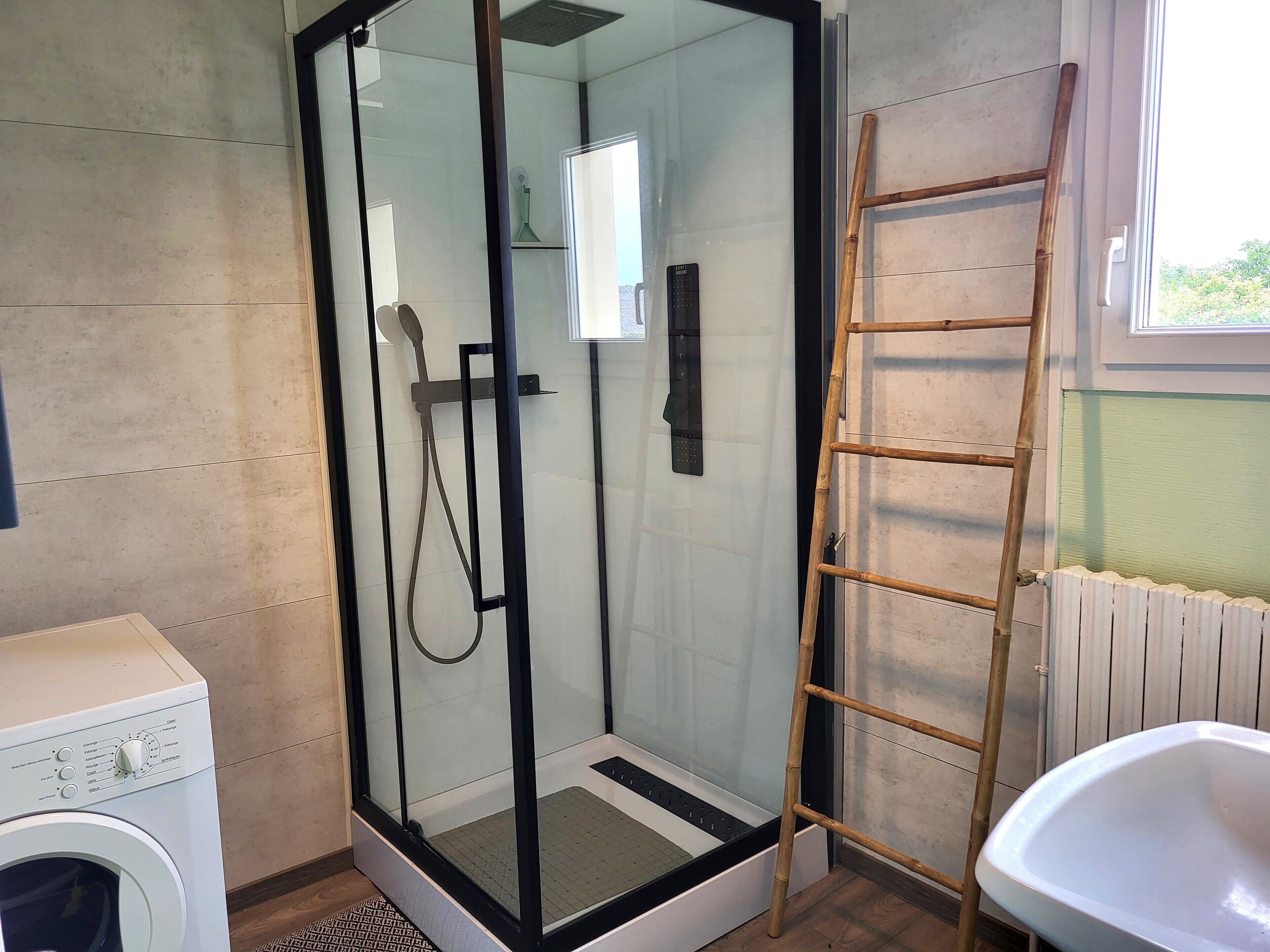 A bathroom with a glass-enclosed shower, a washing machine, a white sink, and a wooden ladder.