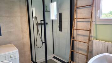 A bathroom with a glass-enclosed shower, a washing machine, a white sink, and a wooden ladder.