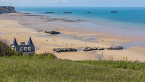 A coastal beach with a distinctive building featuring conical roofs, a sandy shore, and scattered rocks. - Seaside, Les Fleurs Holiday Home with Shared Terrace, Private Garden and Wi-Fi (Créances)