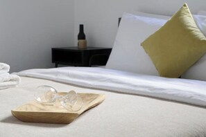 A neatly made bed with a white comforter and a yellow pillow, a wooden tray with glasses, and a bottle on a nightstand. - KAPETAN MATAPA 55, PIREAUS, 185 44 (Pireas)