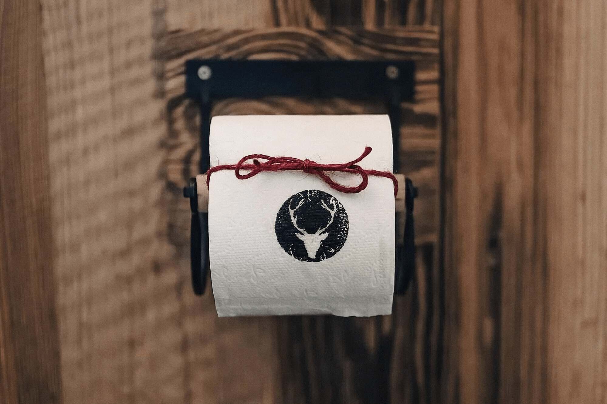 A toilet paper roll with a deer logo, tied with a red string, on a wooden surface.