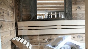 En stuga med träpanel på insidan, en träbänk, en spegel och ett handfat med toalettartiklar.