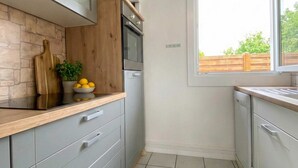 Una cocina con gabinetes grises, encimera de madera, horno integrado y ventana con vistas a la vegetación.