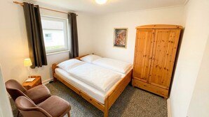 Una habitación con una cama, un armario de madera, una silla, una lámpara y un ventanal con cortinas.