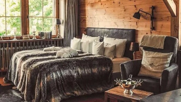Een gezellig houten blokhut slaapkamer met een bed, een bank, een tafel en een raam.