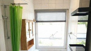 Un baño pequeño y funcional con inodoro, lavamanos y ducha. Una ventana ofrece luz natural y vistas al exterior.