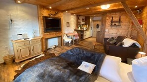 L’intérieur d’un chalet confortable, avec une cheminée, un téléviseur fixé au mur, un coin repas et un canapé agrémenté d’un plaid en fourrure.