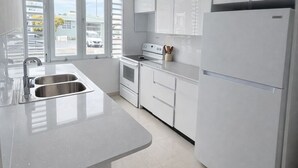 Uma cozinha moderna com armários brancos, uma pia de aço inoxidável, um fogão e uma geladeira.