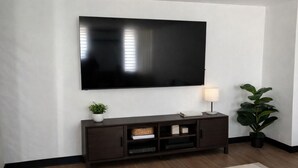 Uma sala de estar moderna com uma TV de tela plana na parede, um móvel de entretenimento em madeira escura abaixo, um abajur e um vaso de plantas.