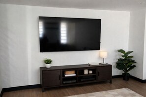 Ein modernes Wohnzimmer mit einem an der Wand befestigten Flachbildfernseher, einer dunklen Holzunterhaltungseinrichtung darunter, einer Stehlampe und einem Topf mit einer Pflanze.