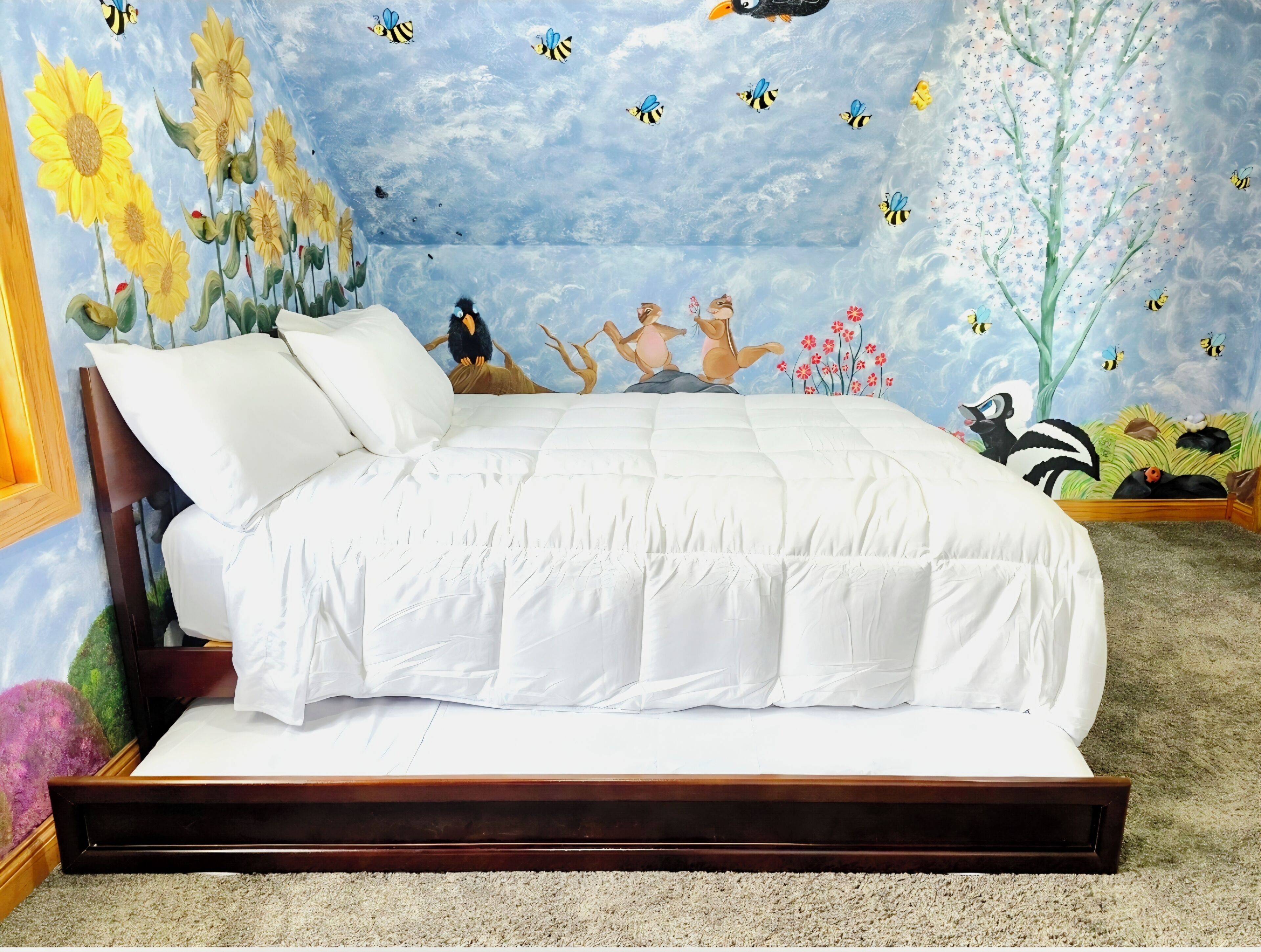 A bedroom with a bed, a wooden headboard, a wall mural, and a carpeted floor.