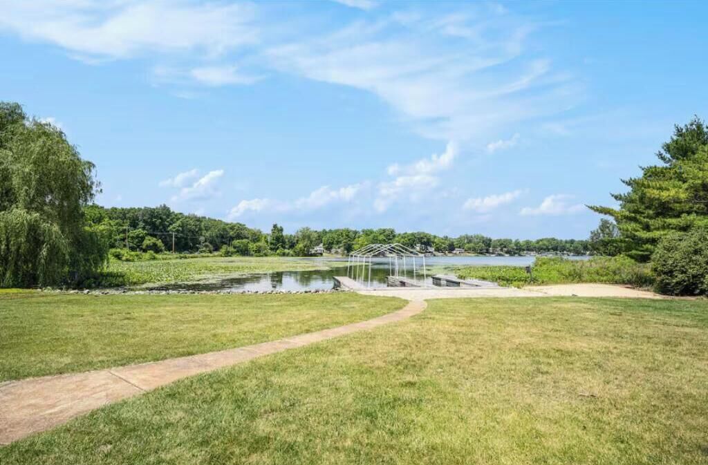 A grassy area with a pond, a covered structure, and a path leading to it.
