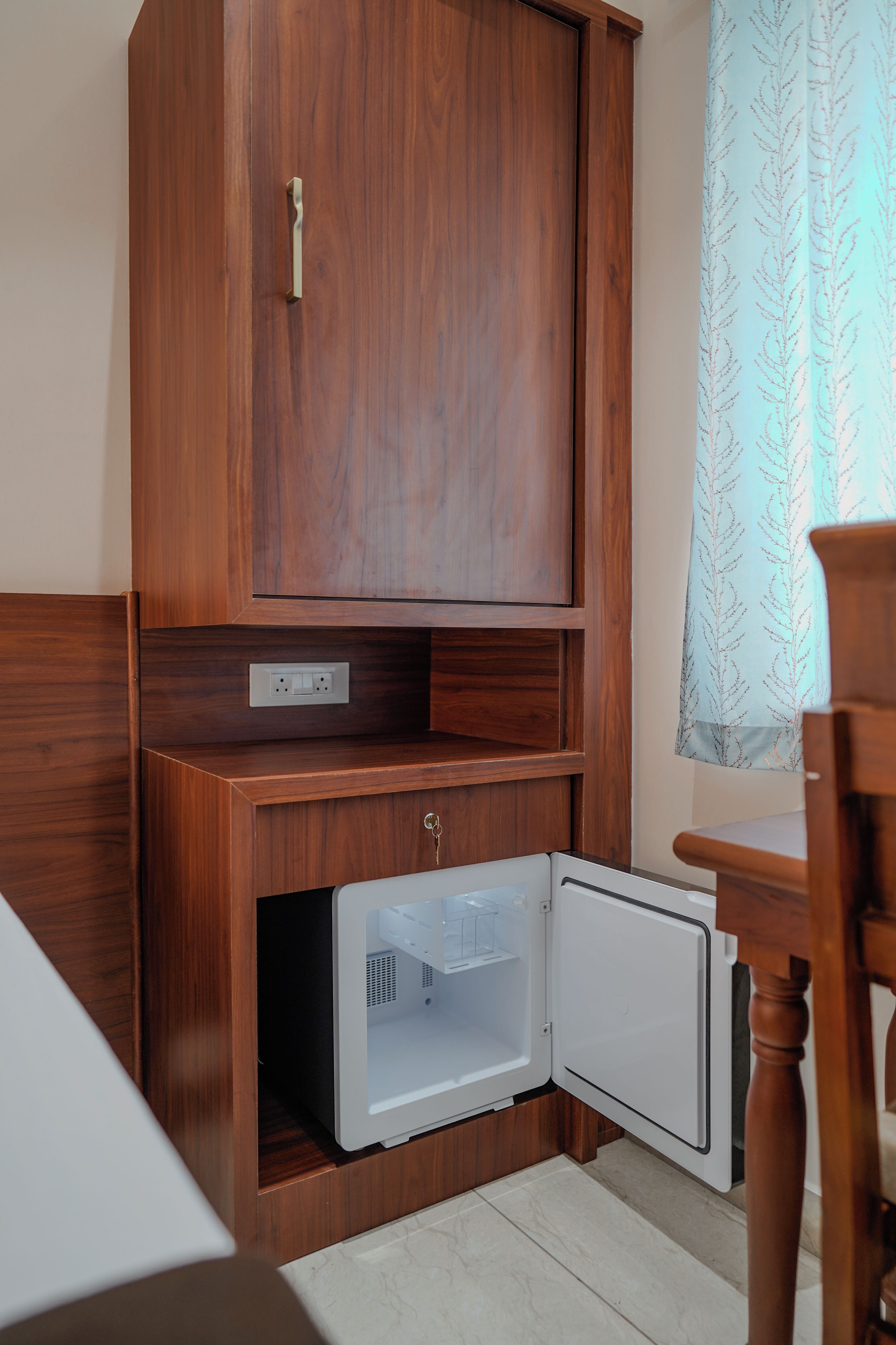 A compact kitchenette with a wooden cabinet, a small fridge, and a dining area with a chair.