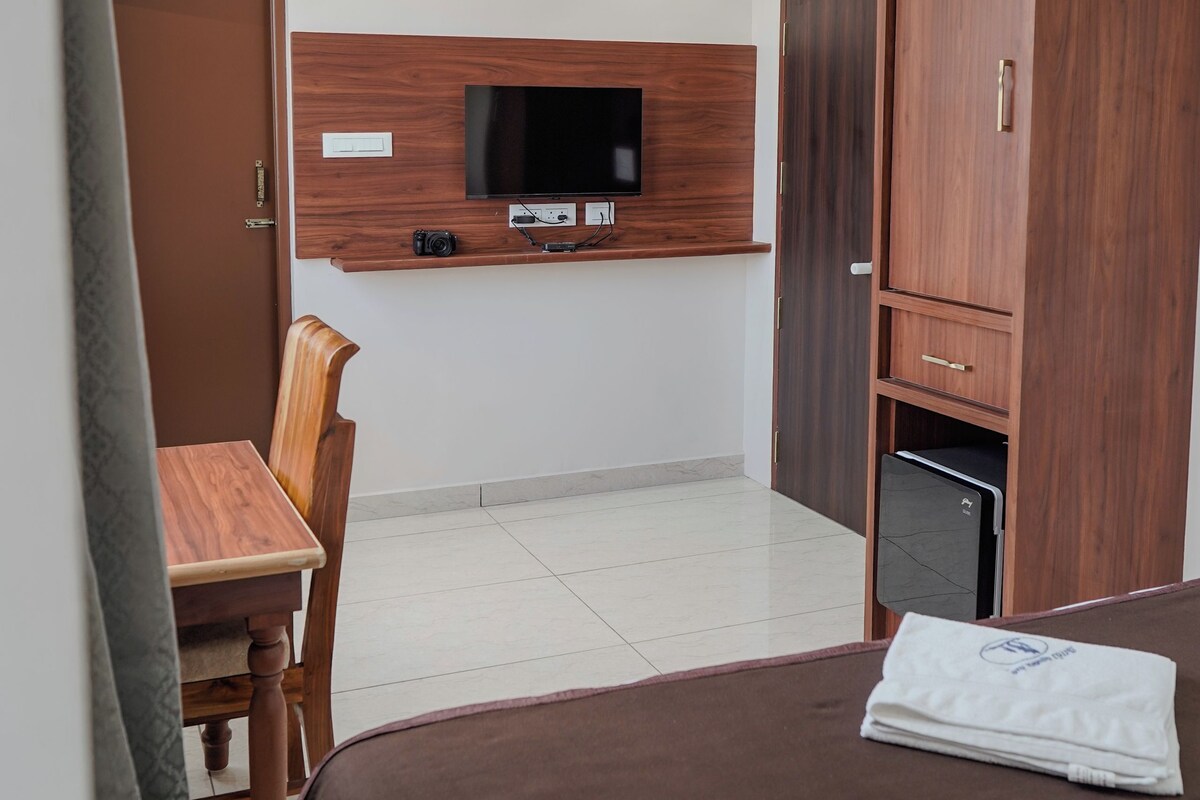 Una habitación de hotel con cama, escritorio, televisor montado en la pared, armario y ventilador de techo.