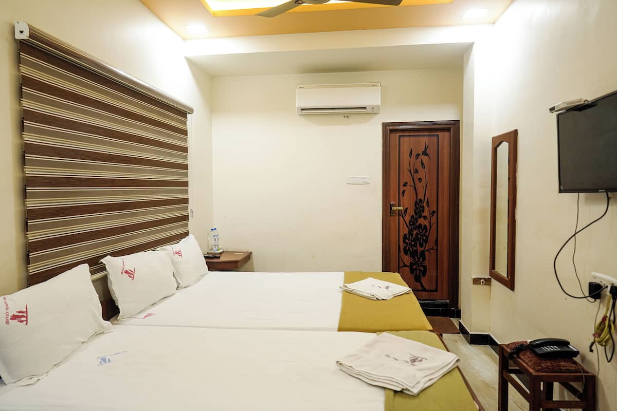 A hotel room with a bed, bedside table, air conditioning unit, and a television.