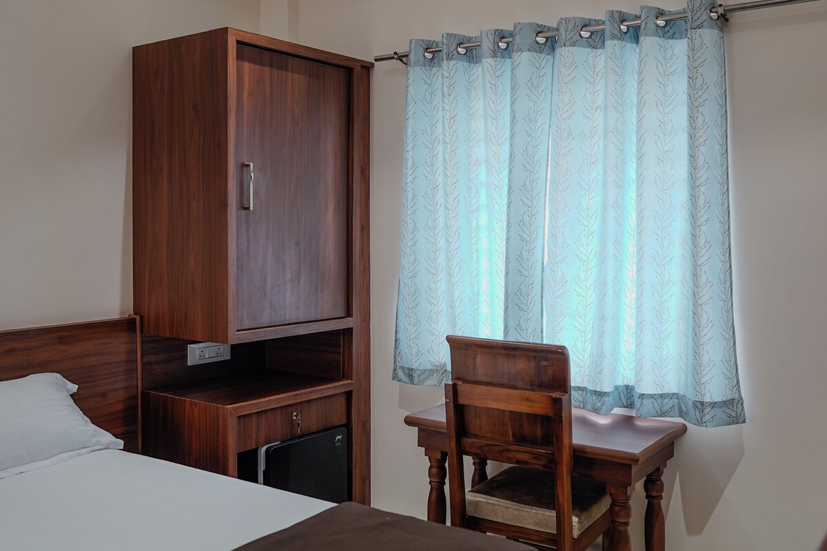 Habitación de hotel con cama, armario de madera, escritorio, silla y ventana con cortinas.