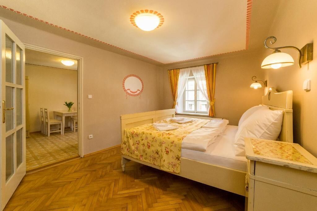 A bedroom with a bed, bedside table, window with curtains, and a door leading to a dining area.