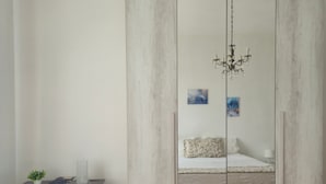 Een slaapkamer met een bed, een stoel, een bureau, een spiegel en een kroonluchter.