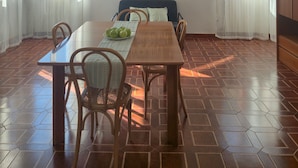 Een eetgedeelte met een tafel, stoelen, een kroonluchter en uitzicht door de ramen.