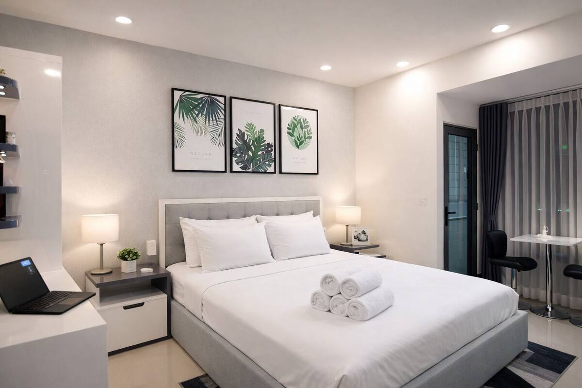 Une chambre d’hôtel moderne, équipée d’un lit, de deux tables de chevet, d’un bureau avec un ordinateur portable, et ornée d’œuvres d’art encadrées représentant des paysages naturels.