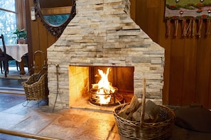 Une cheminée en pierre avec un feu de bois, un panier en osier et un fauteuil.