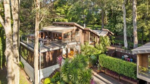 A modern house with a deck, surrounded by lush greenery and tall trees.