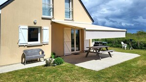 Une maison à deux étages dotée d’un patio couvert, d’une porte-fenêtre coulissante et d’un petit jardin.