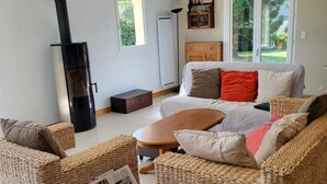 Un salon avec des meubles en osier, une cheminée, un canapé, une table basse et une fenêtre donnant sur un paysage verdoyant.