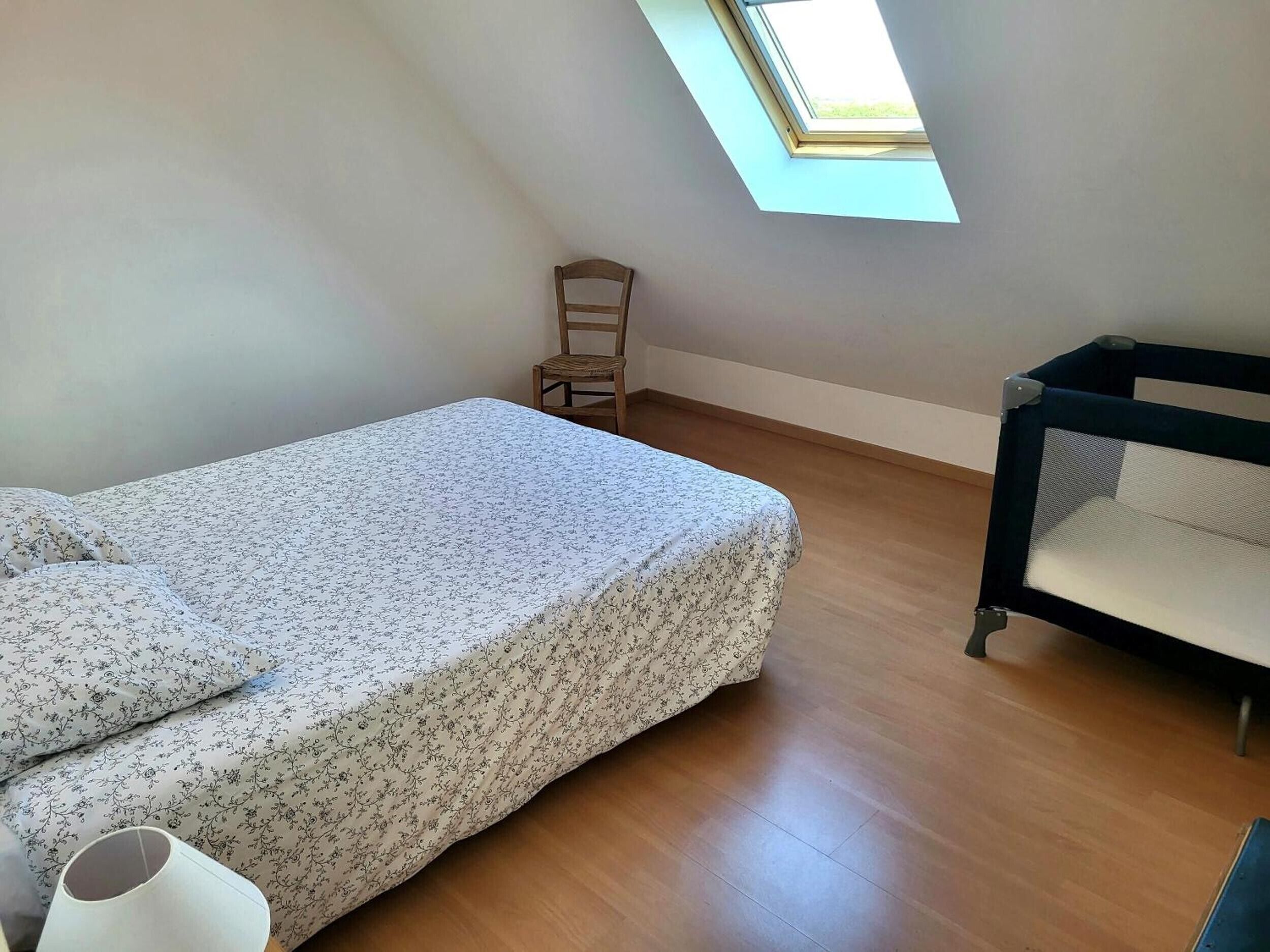 Quarto com cama, cadeira, berço e claraboia.