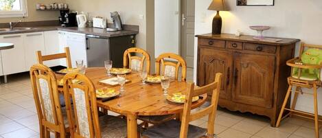 A dining area with a wooden table and chairs, a kitchen in the background, and a staircase.