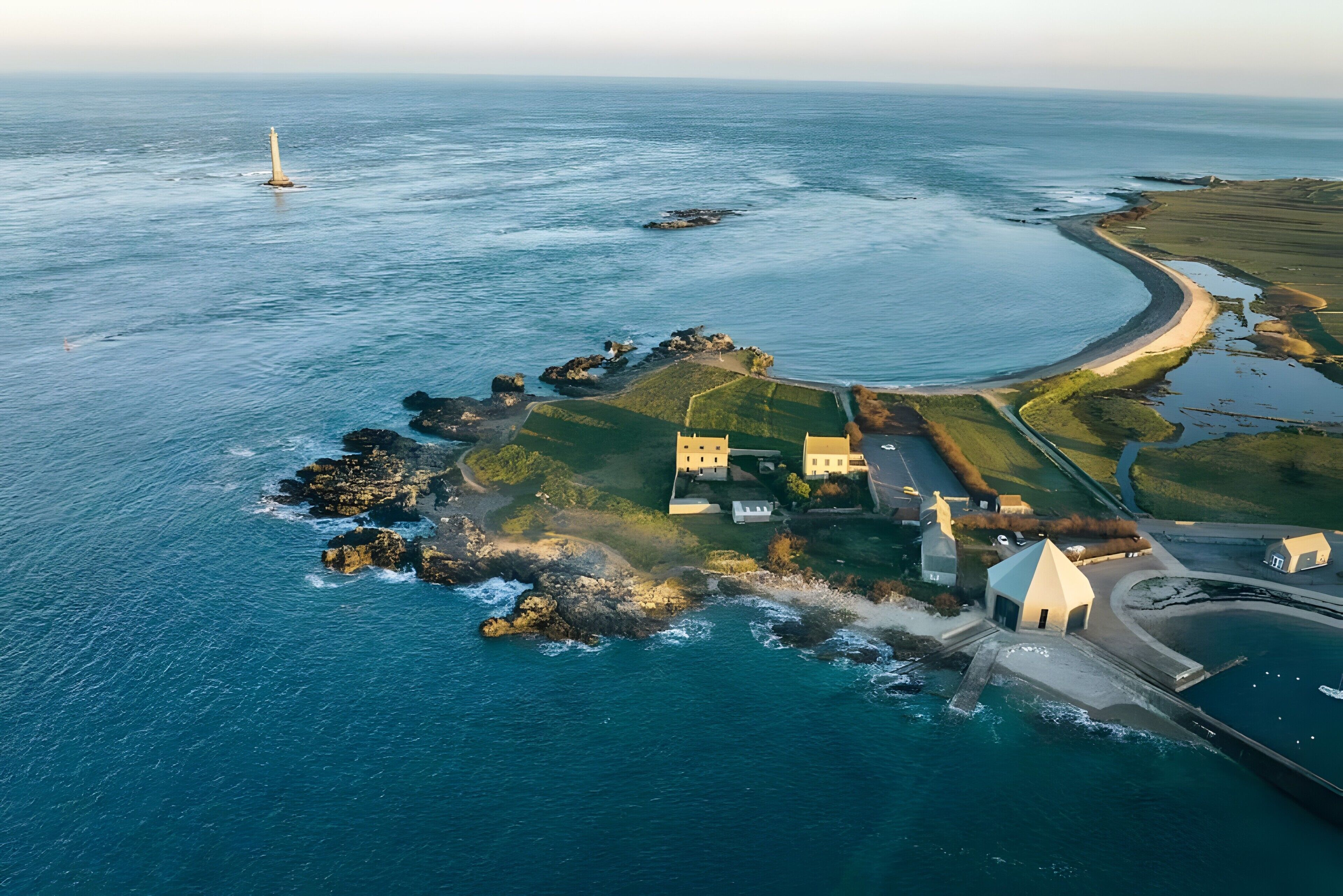 An aerial view of a coastal property with a lighthouse, a winding road, and a mix of buildings and greenery.