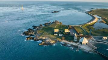 An aerial view of a coastal property with a lighthouse, a winding road, and a mix of buildings and greenery.