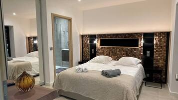 A modern hotel room with a large bed, a bedside table, a mirror, and a wall-mounted TV.