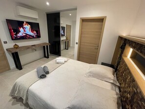 A hotel room with a bed, a TV mounted on the wall, a wooden headboard, and a wooden door.