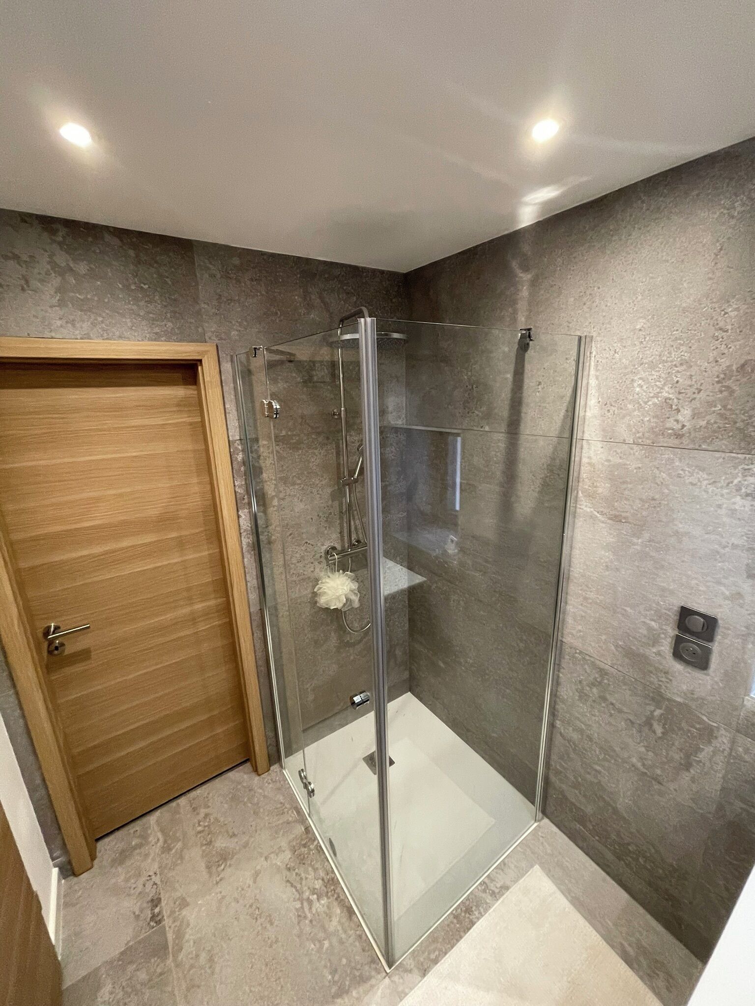 Une salle de bain moderne avec une douche à parois de verre, une porte en bois et un sol en marbre.