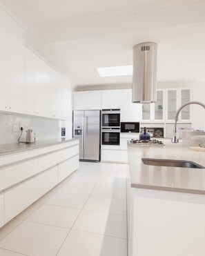 Une cuisine moderne avec des meubles blancs, des appareils électroménagers en acier inoxydable et un puits de lumière.