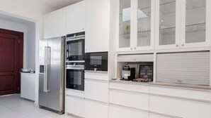 Eine moderne Küche mit weißen Schränken, einem Edelstahlkühlschrank, einem Backofen und einer Kaffeemaschine.