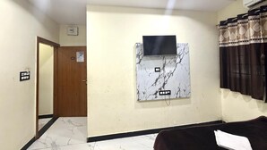 Ein Hotelzimmer mit Flachbildfernseher an einer Wand mit Marmormusterung, einer Holztür und einem dunkelgrauen Sofa.