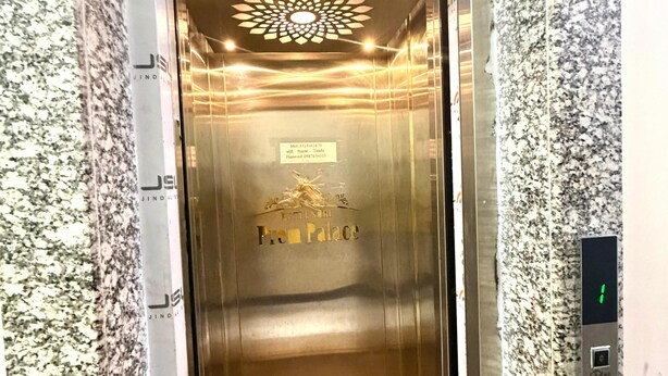 Ein Aufzug mit metallischer Innenausstattung, einem digitalen Display und einem Schild mit der Aufschrift 'Hotel Zen Palace'.