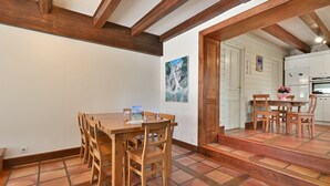 Un comedor con mesa y sillas de madera, una cocina al fondo y suelo de baldosas.