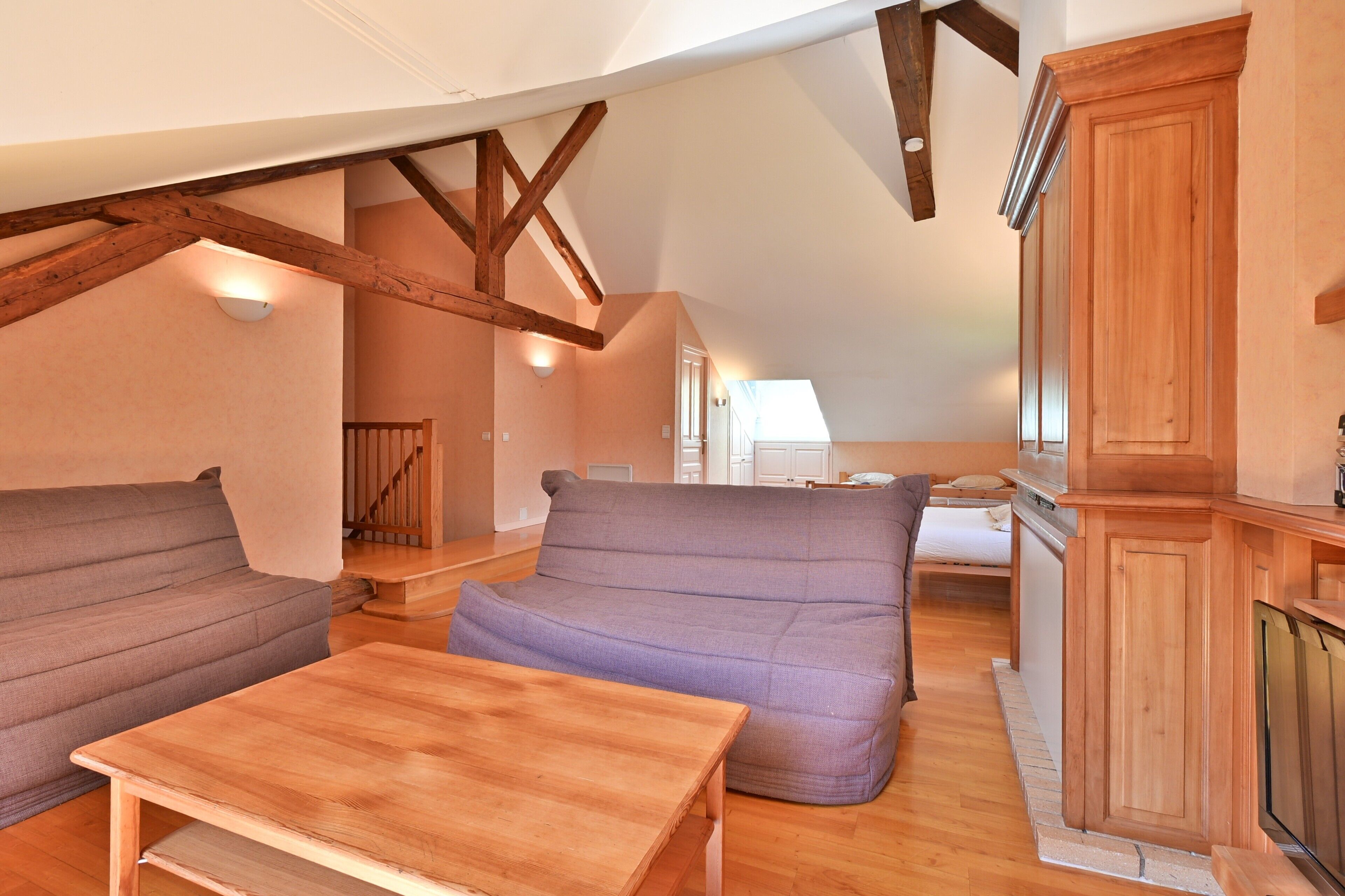 A cozy loft-style room with a wooden table, two sofas, and a kitchen area.