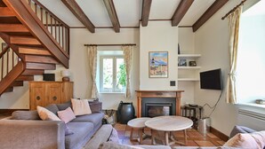 Una sala de estar con escalera de madera, chimenea, televisor y ventana con cortinas.