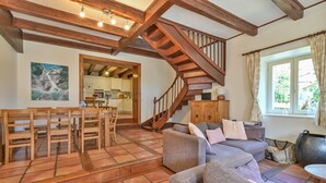 Amplia sala de estar con escalera de madera, mesa de comedor con sillas, sofá y vista a la cocina.