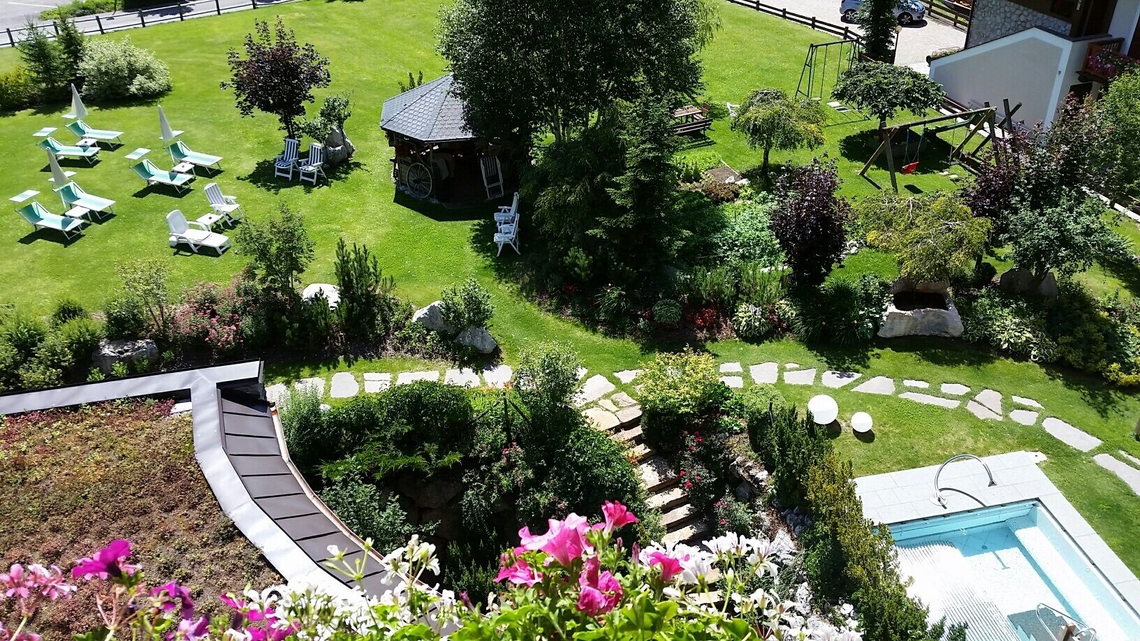 A well-maintained garden with a swimming pool, lounge chairs, and a small wooden structure.