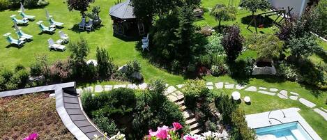 A well-maintained garden with a swimming pool, lounge chairs, and a small wooden structure.