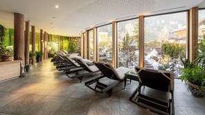 Un espace intérieur lumineux, avec des fauteuils confortables, de grandes fenêtres et des plantes d’intérieur.
