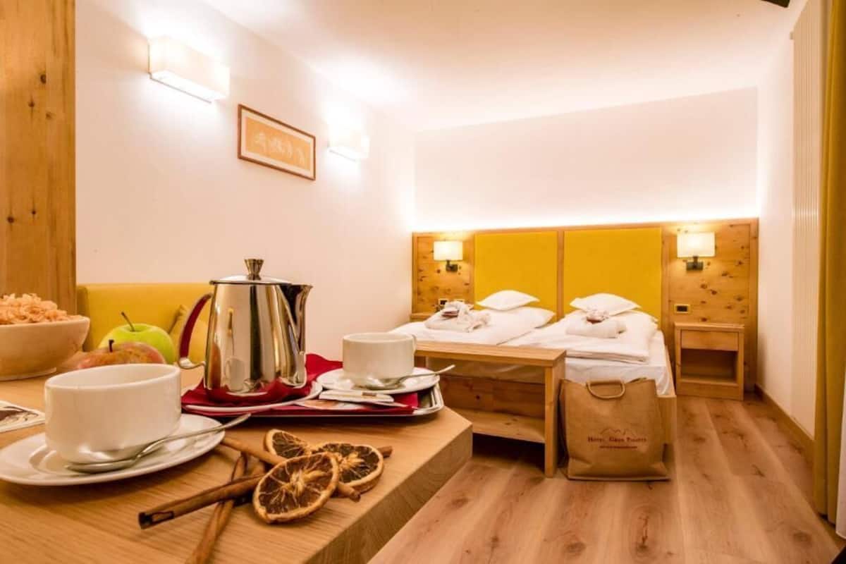 Habitación de hotel con cama de madera, mesitas de noche, una mesa para el desayuno y suelo de madera.