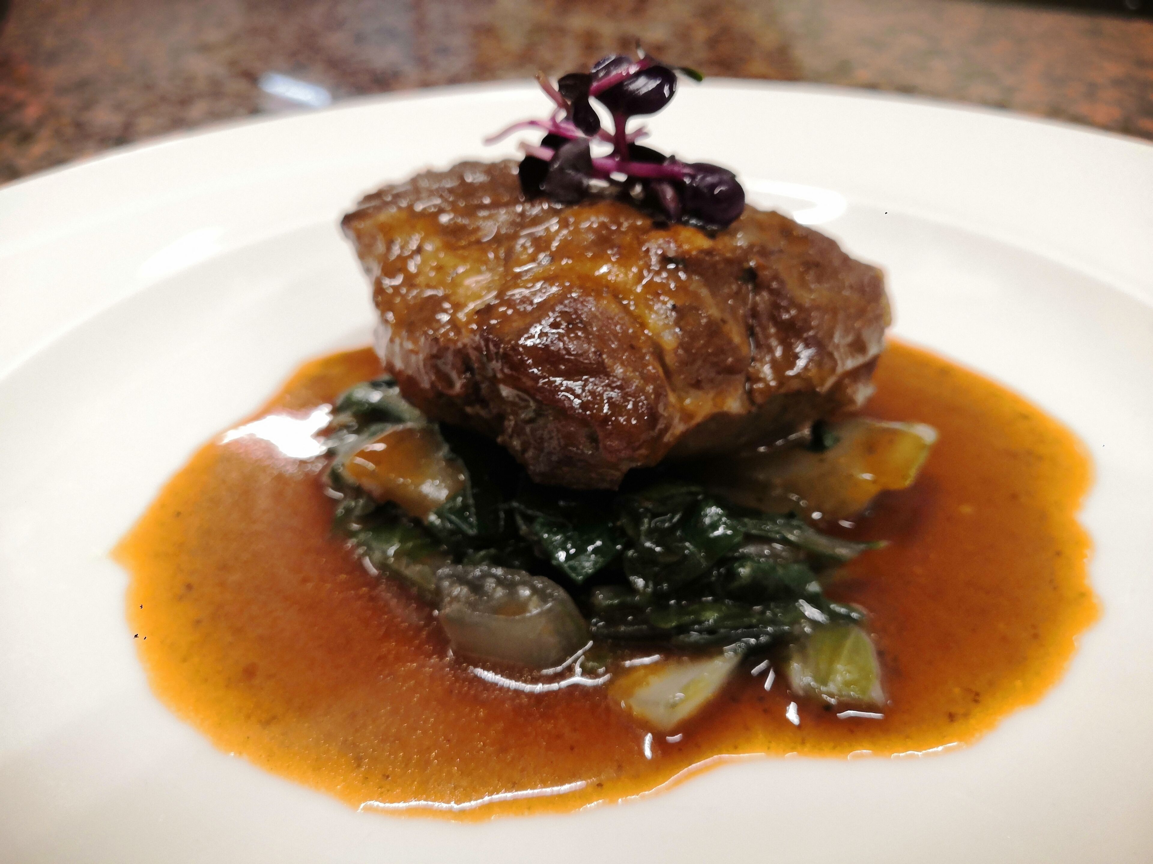 A plate with a piece of meat, greens, and a sauce.