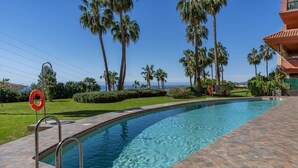 A swimming pool with metal ladders, surrounded by palm trees and a clear sky. - Apartment 'Estilo El Higuerón' with Sea View, Wi-Fi, and Air Conditioning (Benalmádena)