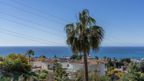 A coastal residential area with houses, a palm tree, and the ocean in the background. - Apartment 'Estilo El Higuerón' with Sea View, Wi-Fi, and Air Conditioning (Benalmádena)